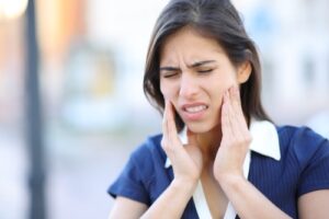 Woman holding her jaw in pain from TMJ disorder and in need of cosmetic dentistry.